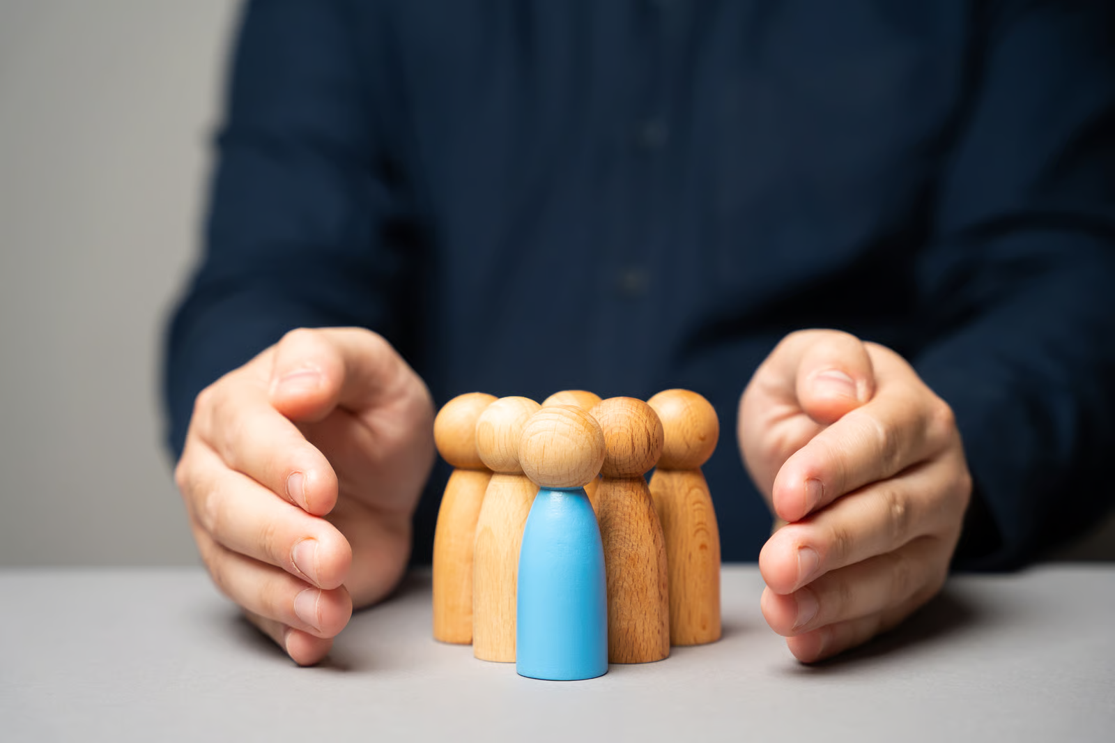 Awareness & Auflagen — schützende Hände um Holzfiguren, eine blau hervorgehoben als Symbol für Sensibilisierung und Schutz